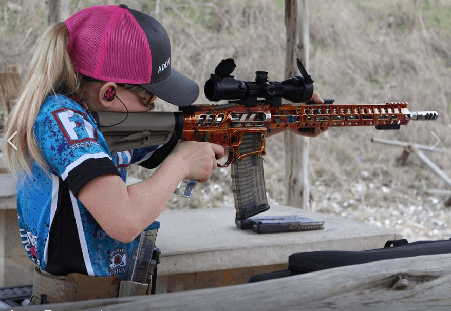 A girl wearing a pink hat is aiming at a rifle while using custom hearing protection.