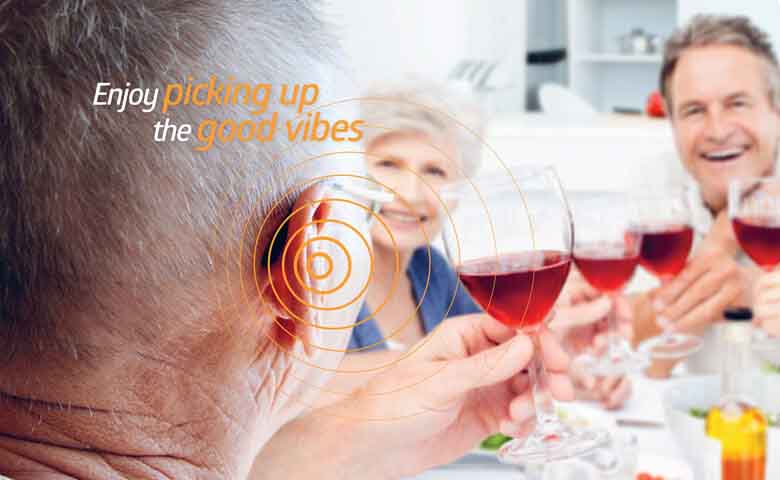 A group of people drinking wine at a dinner table, wearing hearing aids.