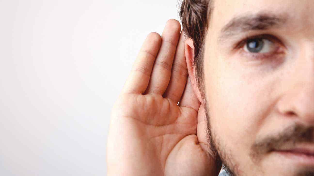 A man is holding his hand to his ear indicating that he is having trouble hearing and his need to know about trends in hearing protection.