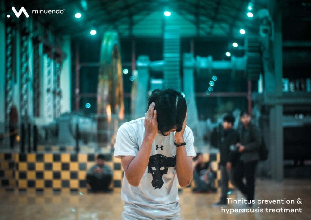 A man is holding his head up in front of a building because he is suffering from tinnitus or Hyperacusis.